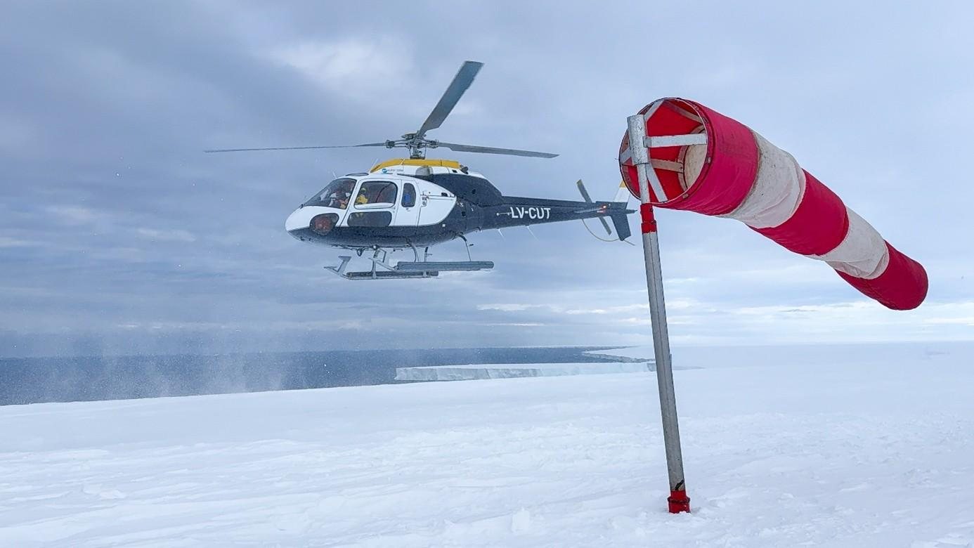 Hubschrauber im Landeanflug neben einem Windsack auf dem antarktischen Eis
